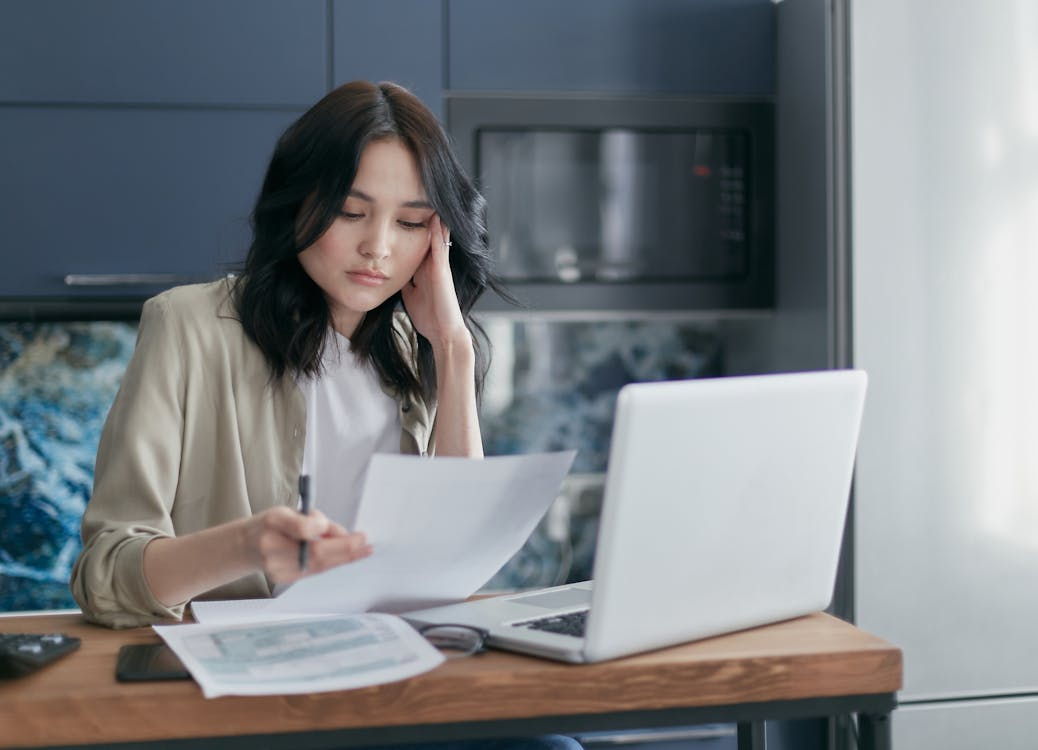 Woman reviews hidden fees on monthly bills while checking paperwork beside a laptop.