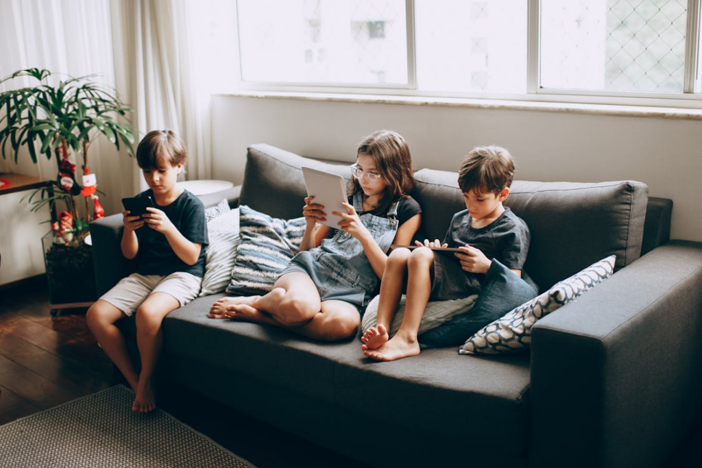 Children using tablets on a couch with the best internet plan for multiple devices at home.
