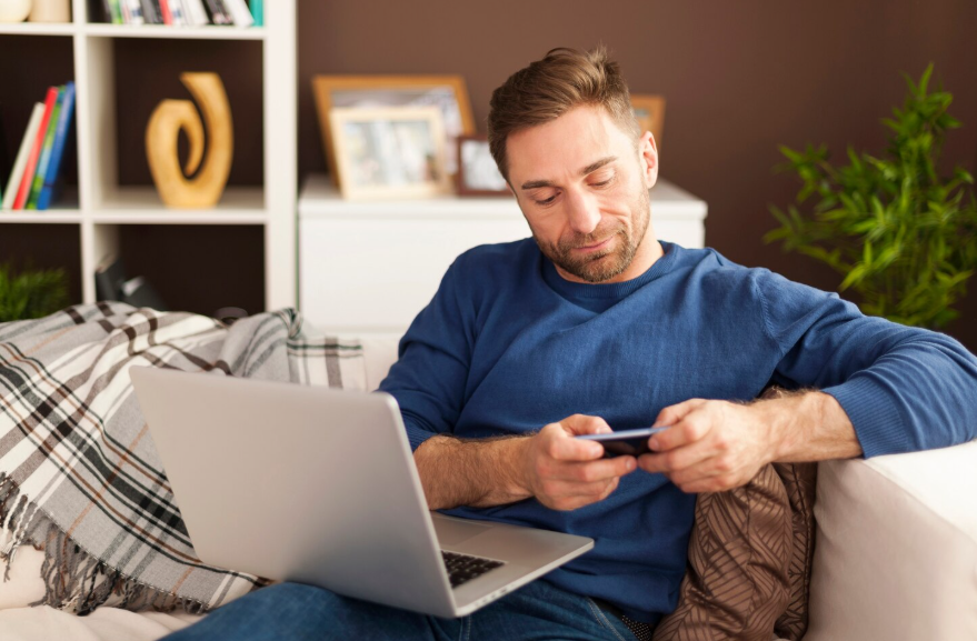Man using a laptop and phone to compare a single person phone and streaming plan at home.