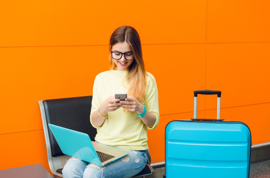 Traveler uses the best phone plans for travelers while checking her phone beside luggage.